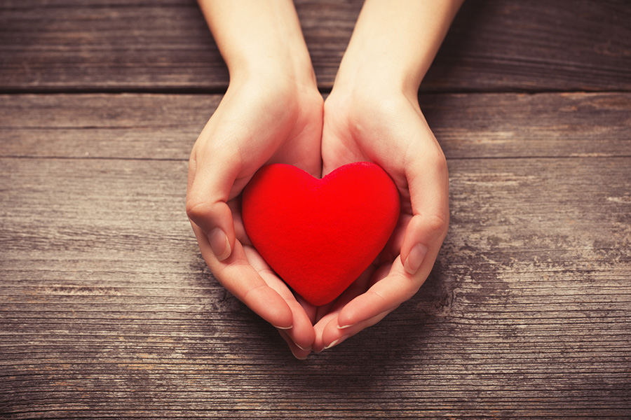 Two open hands cupping a red heart